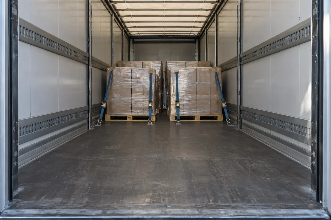 Interior de un tráiler a medio cargar con los palets bien sujetos y luz entrando por las puertas abiertas.